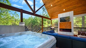 A hot tub on a deck with a view of trees, a fireplace, and a seating area. - Sugar Bear Den Stay for 10! (Broken Bow)