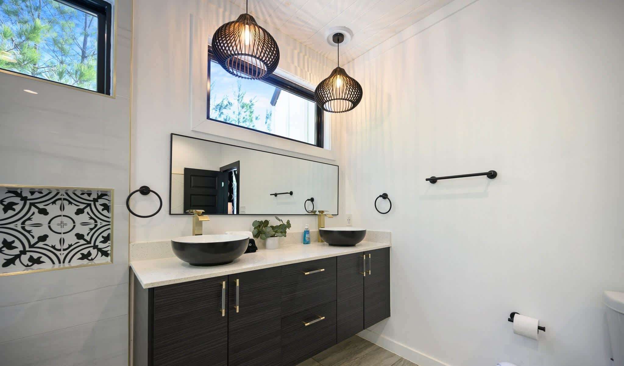 A modern bathroom with two sinks, dark cabinetry, a large mirror, and pendant lights.