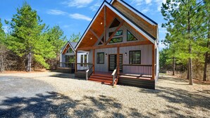 A modern log cabin with a prominent gable roof, large windows, and a wooden deck. - Sugar Bear Den Stay for 10! (Broken Bow)