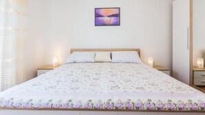 Een slaapkamer met een bed, twee nachtkastjes, een wanddecoratie en een raam met dunne gordijnen.