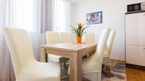 Een eethoek met een houten tafel en witte stoelen, een bloempot en een schilderij aan de muur.