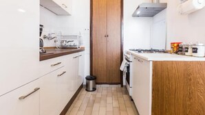 Een compacte keuken met witte kastjes, een houten deur, een fornuis en een koffieapparaat.