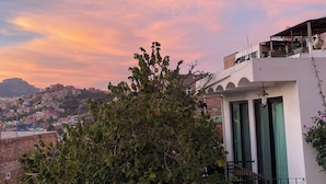 Un edificio residenziale con un balcone, un albero sullo sfondo e una vista lontana di una città.