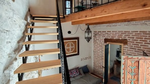 Una scala in legno con ringhiera nera conduce a una zona mansardata con parete in mattoni e un settimino in legno.
