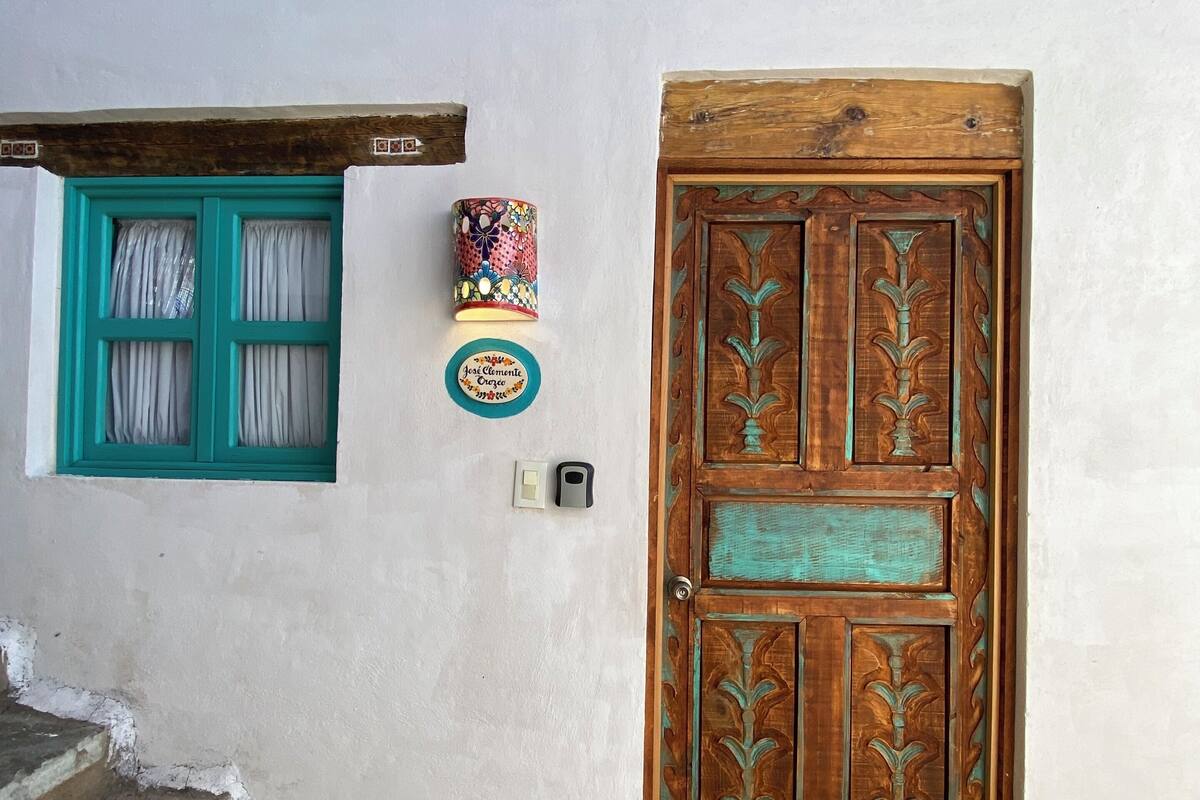 A wooden door with intricate carvings, a teal-framed window, and a small wall-mounted light fixture.