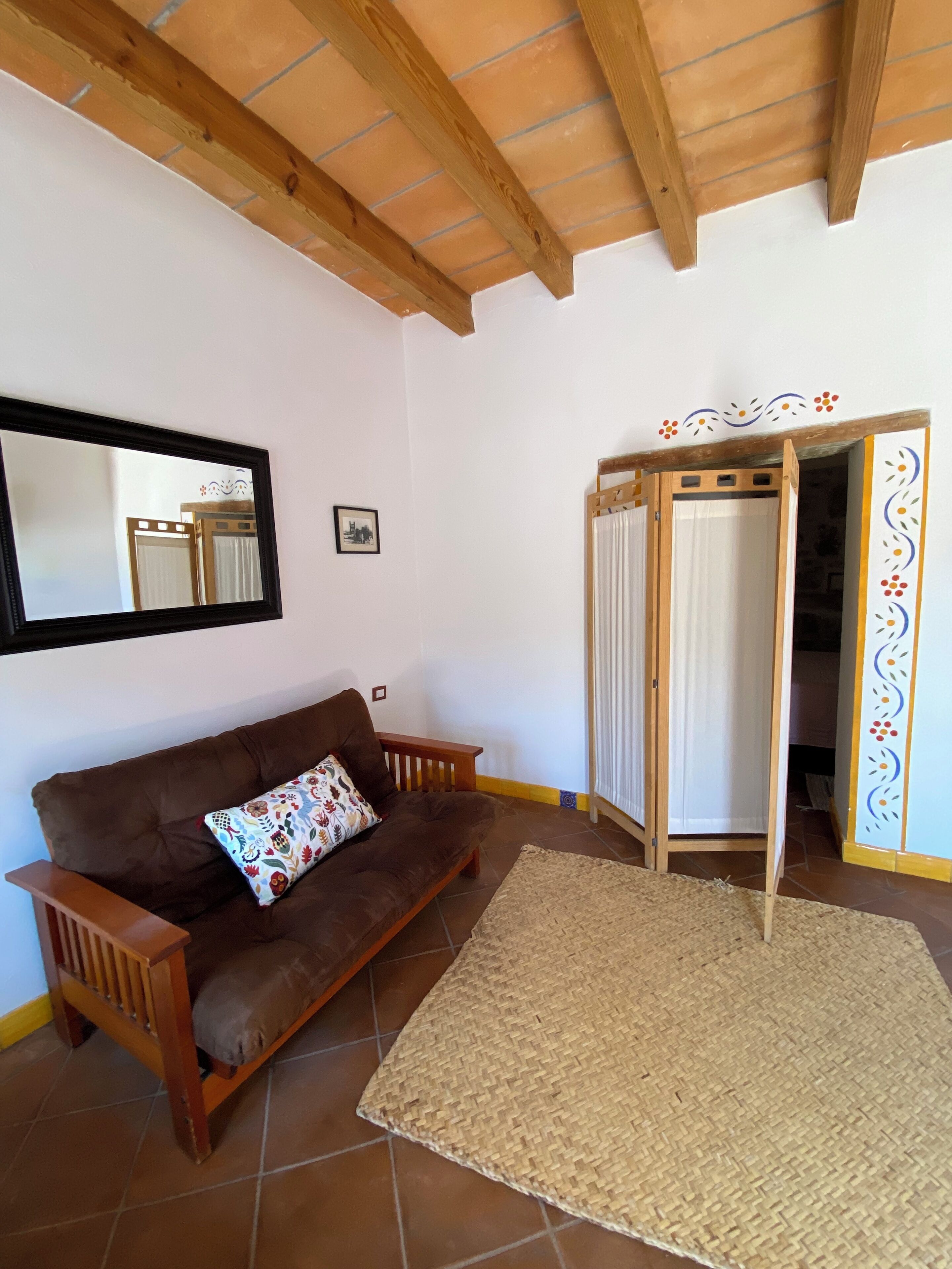 Une pièce comprenant un canapé marron, un tapis tissé, un banc en bois, un miroir et une armoire ornée d’un panneau décoratif.