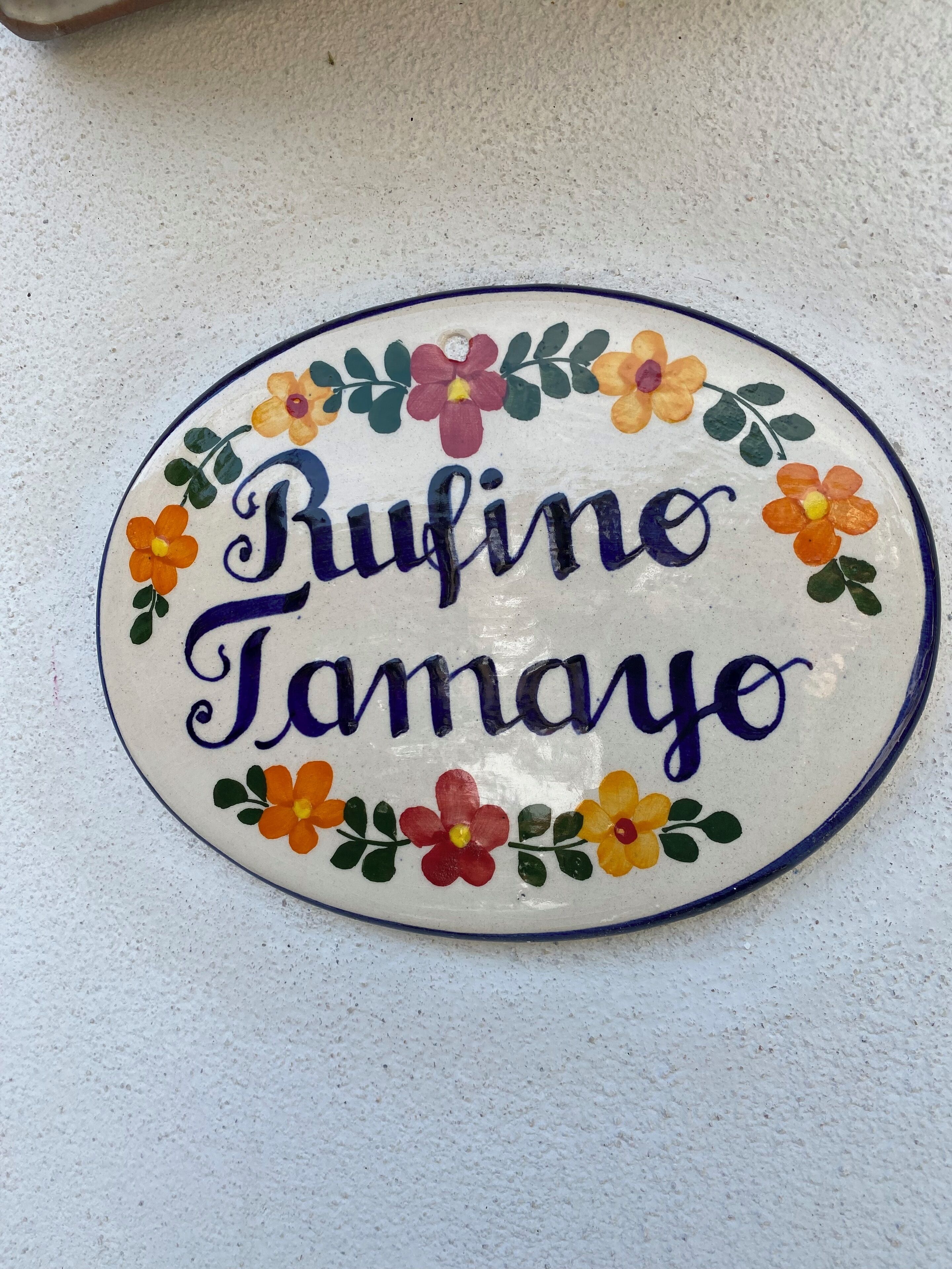Koristeellinen lautanen, jossa on nimi ”Bufino Tamayo” ja sen ympärillä värikkäitä kukkia.