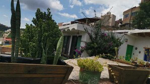 Un giardino pensile con piante in vaso, una panchina di legno e un edificio con una porta verde.