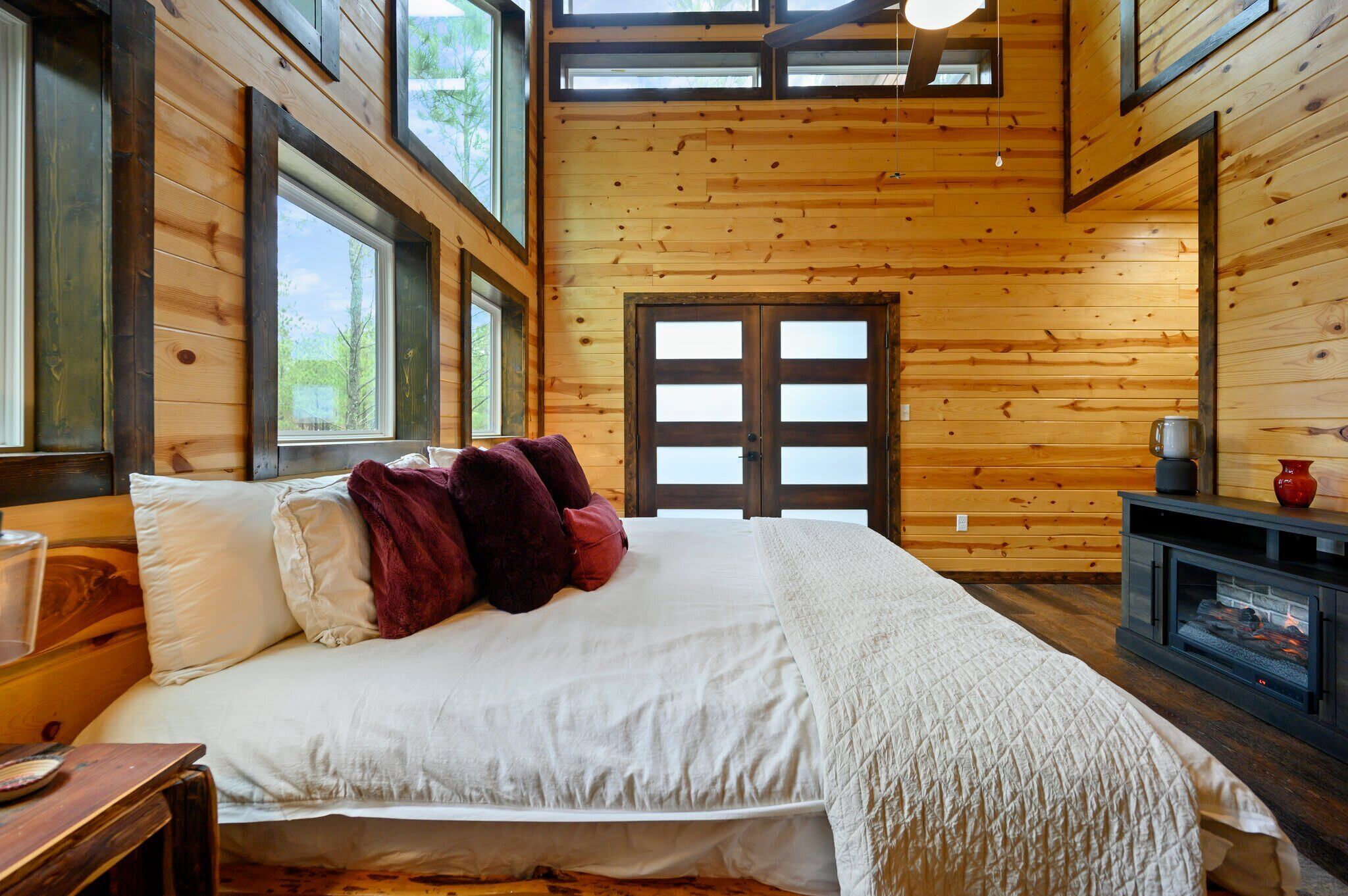 Une chambre à coucher dans un chalet en bois, avec un lit, une cheminée et de grandes fenêtres.