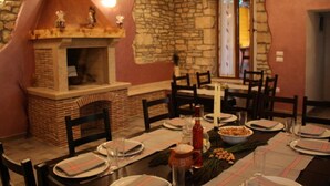 Un espace repas agrémenté d’un mur en pierre, de poutres en bois au plafond et d’une cheminée en briques.