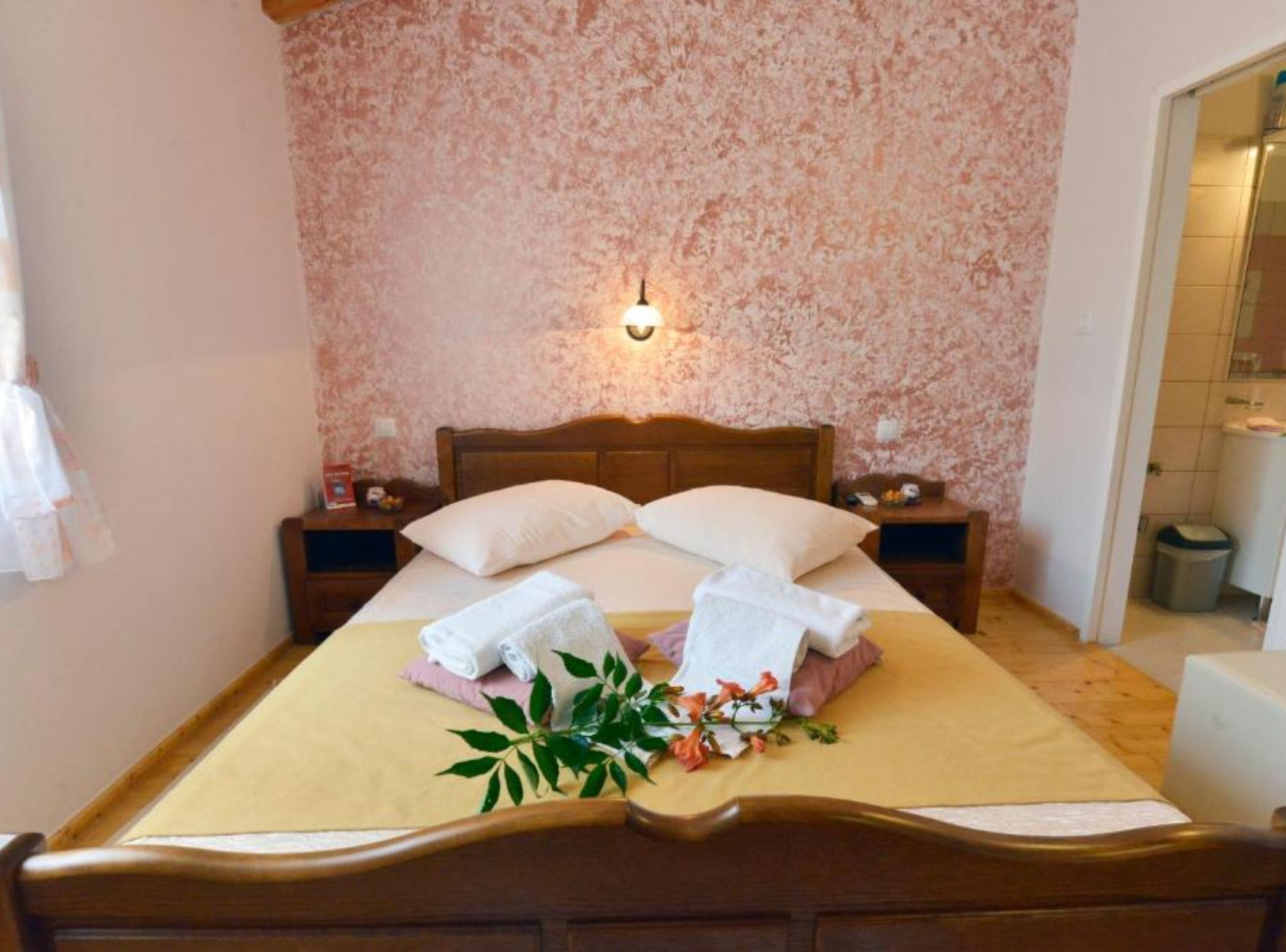 A neatly made bed with towels and a floral arrangement, a wooden headboard, and a wall-mounted light fixture.