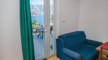 A room with a blue sofa, a dining table, and a view of a mountainous landscape through a sliding glass door.