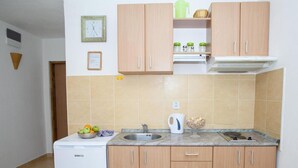 A compact kitchen with wooden cabinets, a built-in sink, a white refrigerator, and a tiled backsplash. - Charming Seaside Escape in Kotor (Donji Stoliv)