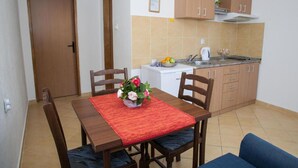 A compact kitchen with wooden cabinets, a sink, and a small refrigerator. There is a dining table with chairs and a vase of flowers. - Charming Seaside Escape in Kotor (Donji Stoliv)