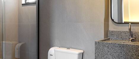 Une salle de bain moderne comprenant des toilettes, une douche à parois de verre et un comptoir en granit avec un évier et un miroir.