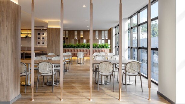 A modern dining area with wooden partitions, metal chairs, and a view of the city through large windows. - Villano Hotel (Blumenau)