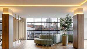 A modern lobby with a large window, a sectional sofa, and a potted plant. - Villano Hotel (Blumenau)