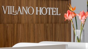 A reception desk with a wooden panel wall and the text "VILANO HOTEL" above it. - Villano Hotel (Blumenau)
