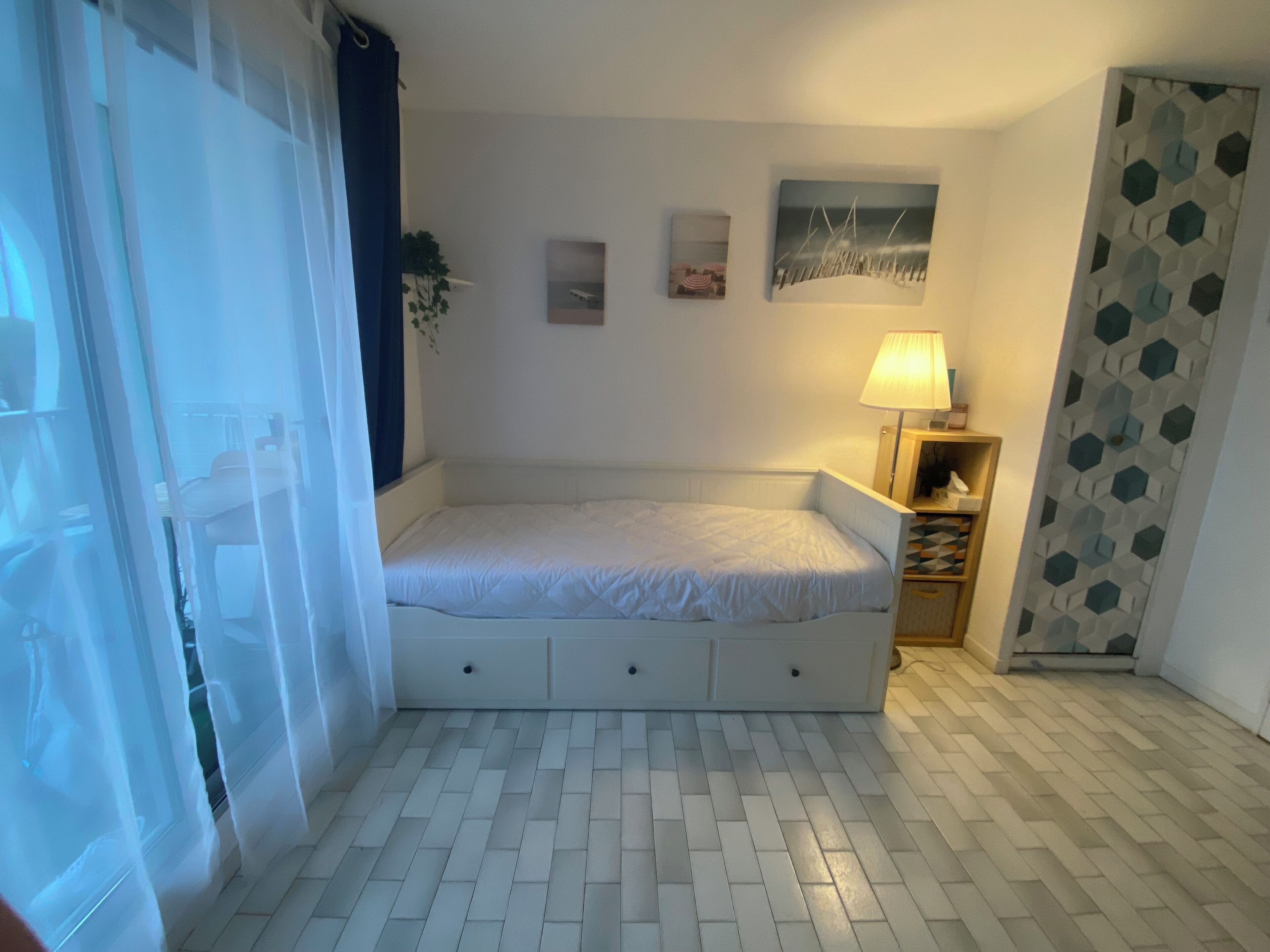 A bedroom with a bed, a nightstand, a lamp, and a wall with two pictures.