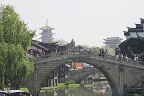 A stone bridge over a calm water body with traditional architecture in the background. - Minhua Business Hostel (Shanghai)