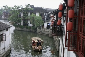 A narrow waterway with traditional buildings on either side, a boat with a person rowing, and red lanterns hanging from the building.