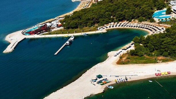 An aerial view of a coastal resort with a marina, beach, and pool area.