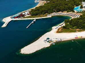 Vista aérea de un complejo turístico costero con puerto deportivo, playa y zona de piscina.