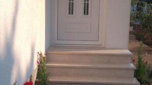 A white door with a small window, a set of concrete steps, and potted plants.