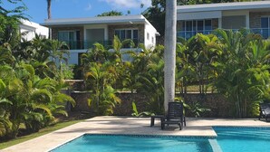 A modern hotel with a swimming pool surrounded by lush tropical vegetation. - Luxurious 1-bedroom condo in Sosúa with AC, WiFi, Backyard, Terrace, and Balcony (Sosúa)
