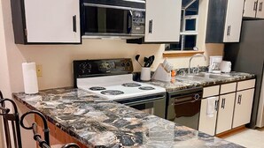 A compact kitchen with a central island, a microwave, a stove, and a sink. - Cozy 2-bedroom condo- right beside SCD (Branson)