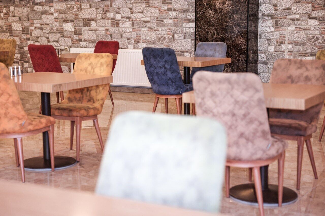 A restaurant with multiple tables and chairs, featuring a stone wall backdrop.