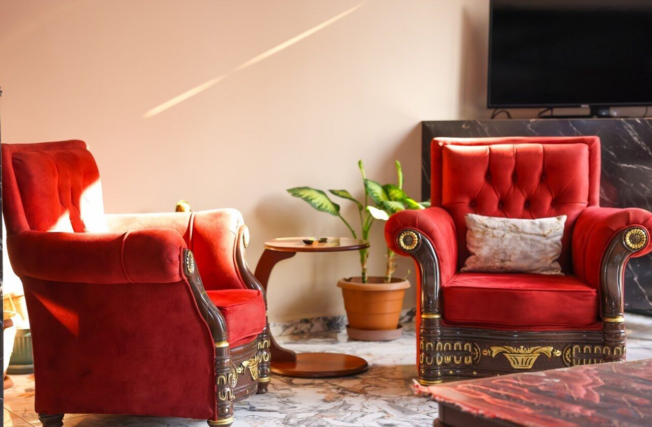A room with two red velvet armchairs, a small wooden side table, a potted plant, and a marble floor.