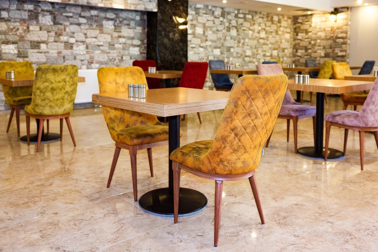 Un interior de restaurante con paredes de piedra, varias mesas y sillas con diferentes colores de tapicería.