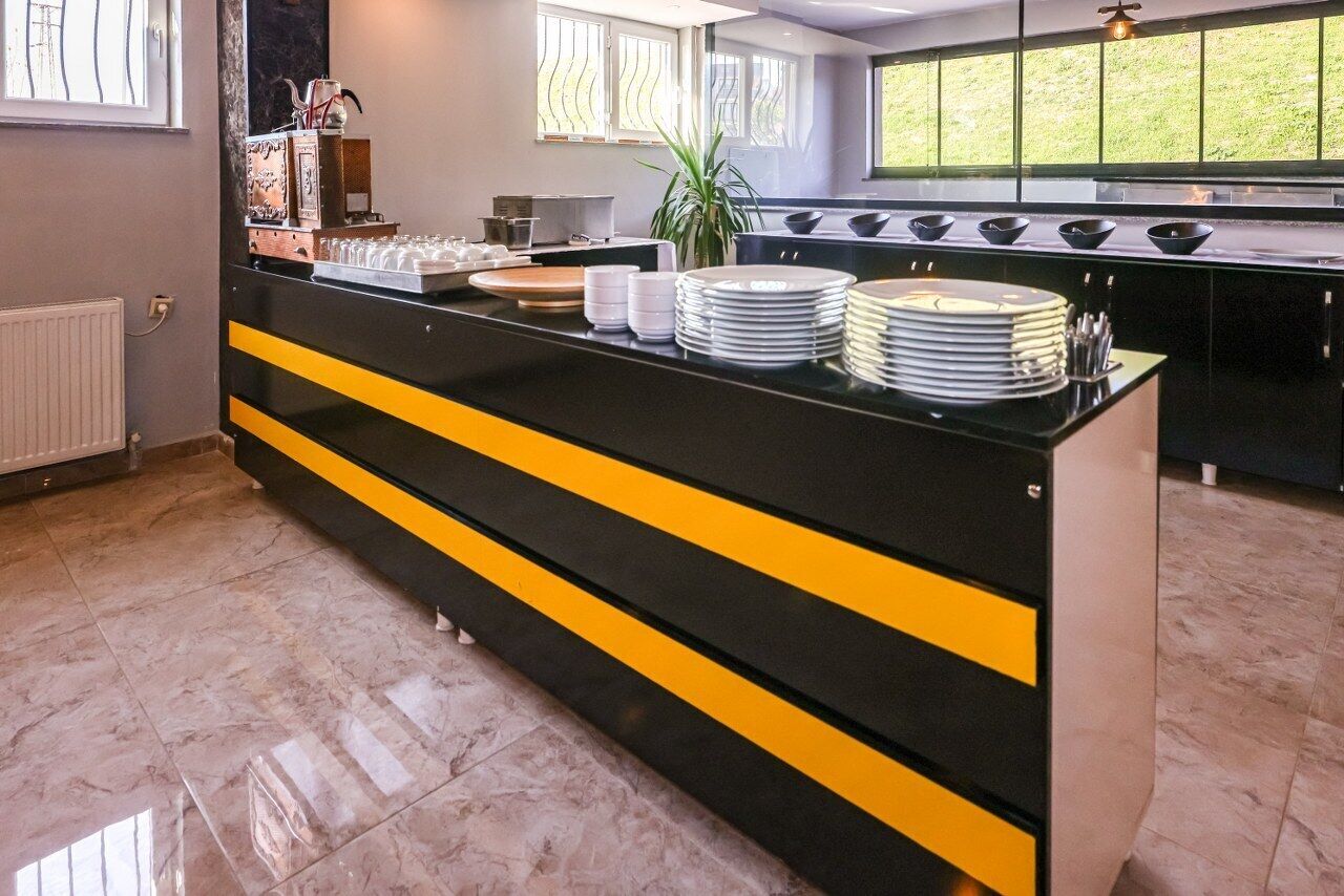Una cocina moderna con encimera negra y amarilla, platos y cuencos blancos, y una planta en maceta.