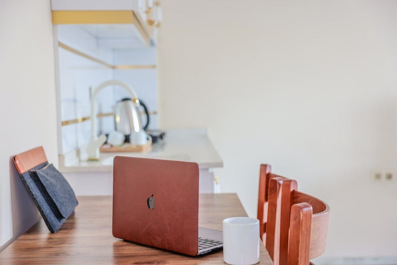 Um laptop sobre uma mesa de madeira, com uma caneca branca e uma cadeira.