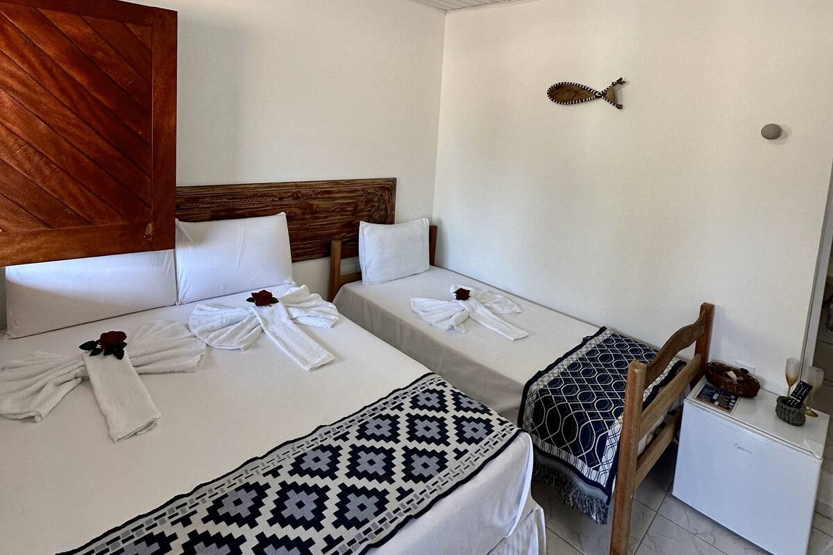 Ein Hotelzimmer mit zwei Betten, einem Holzkopfende, einer weißen Decke und einem kleinen Nachttisch mit Fernbedienung und einem Glas.