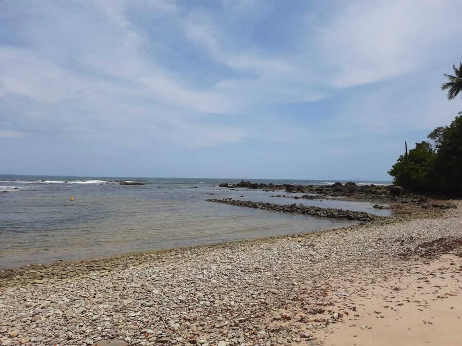 Uma praia de pedras com águas calmas e céu claro.