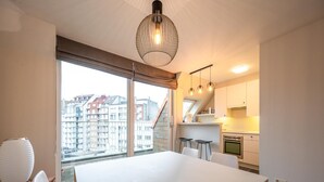 A modern kitchen with white cabinets, a built-in oven, and a dining area with a white table and chairs. - Duplex in Knokke-heist Near the Beach (Knokke-Heist)