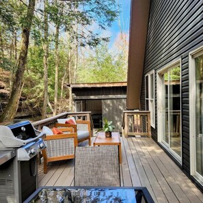Een terras met buitenmeubilair, een barbecue en uitzicht op het omliggende bos.
