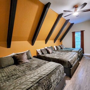 Habitación de hotel con tres camas, un ventilador de techo y una ventana con cortinas.