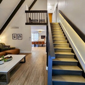 Un interior moderno con una escalera, suelo de madera y una zona de estar con sofá y mesa de centro.