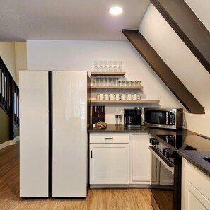 Una cocina moderna con un refrigerador blanco, una cafetera, un microondas y una estantería con cristalería.