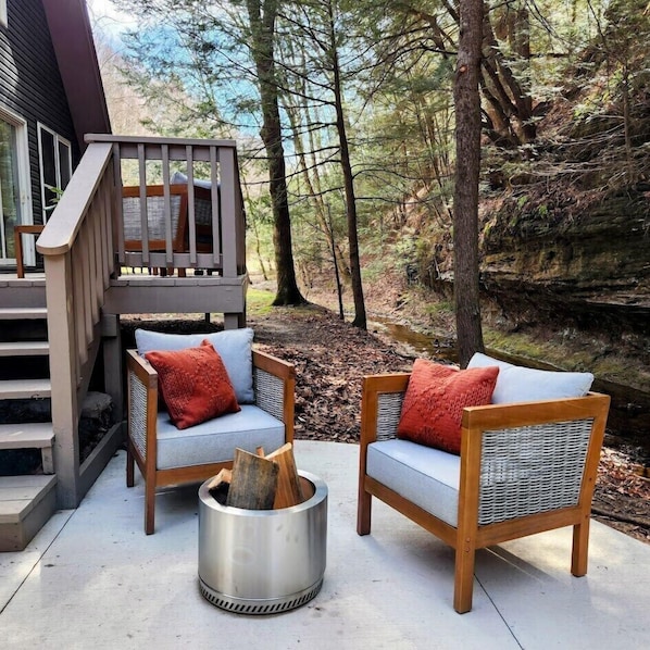 A deck with two wicker chairs, each with a cushion, and a metal fire pit.