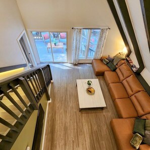 A modern living room with a wooden floor, a brown leather sofa, a white coffee table, and a staircase with a black railing.