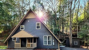 A two-story cabin with a front porch, a small attached shed, and a gravel driveway.