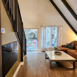 A modern living room with a wooden floor, a sofa, a coffee table, and a staircase leading to an outdoor area. - RockFall Retreat! Nature's Haven (Lancaster)