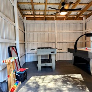 Una habitación con mesa de ping pong, mesa de futbolín y un estante con equipo deportivo.