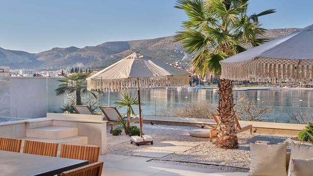 A rooftop terrace with a pool, lounge chairs, and a dining area overlooking a mountainous landscape.