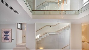 A spacious living area with a staircase leading to an upper floor, a glass railing, and a minimalist design.