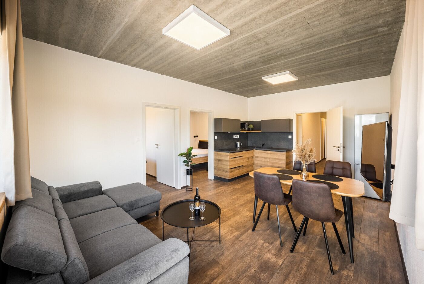 Un salon moderne avec un canapé d’angle gris, une table basse ronde et un coin repas comprenant une petite table et des chaises.